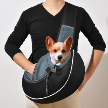 Small dog looking out of the mesh opening of a black and grey pet sling carrier